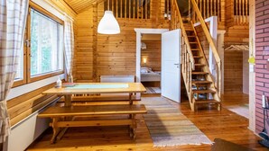 Interior de una cabaña de madera con comedor, escalera y habitación.