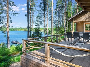 Une terrasse en bois, agréée de mobilier d’extérieur, qui offre une vue sur un lac et est entourée de grands arbres.