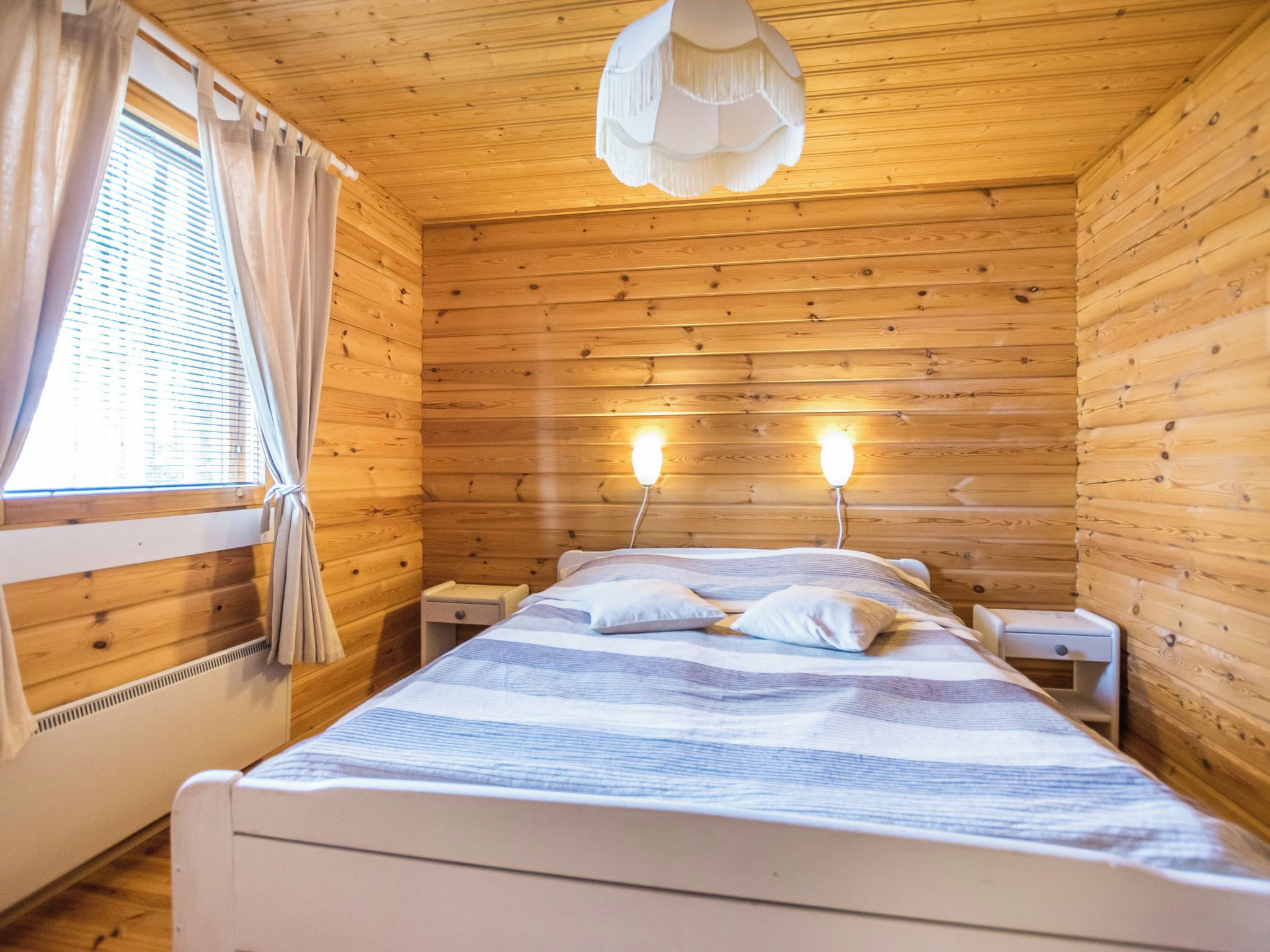 Un dormitorio de cabaña de madera con una cama, mesitas de noche y un ventanal con cortinas.
