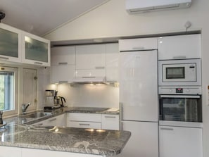Una cocina moderna con muebles blancos, encimera de granito, cafetera y electrodomésticos integrados, incluyendo un microondas y horno.