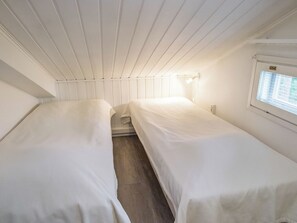 A small, single-room accommodation with two beds, a window with blinds, and a wall-mounted light fixture.