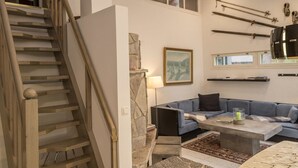 A modern living room with a wooden staircase, a blue sofa, a coffee table, and a stone accent wall.