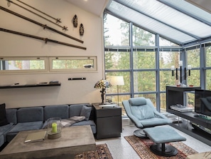 Una sala de estar moderna con un ventanal grande, un sofá, un sillón reclinable, una mesa de centro y una lámpara.