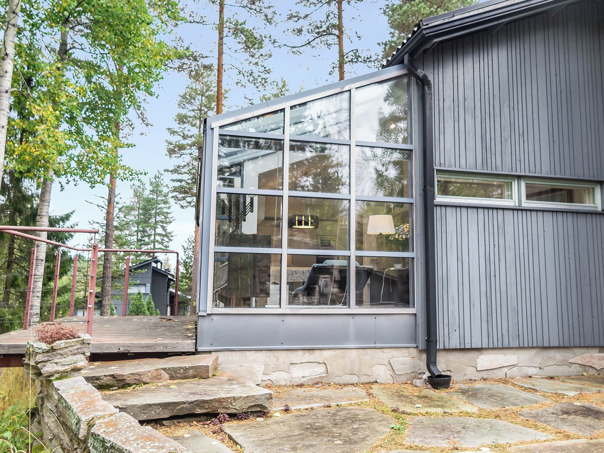 A modern building with a large glass window and a stone staircase leading to a wooden deck.