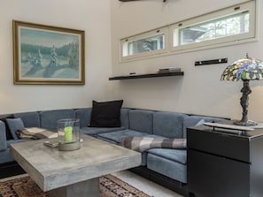 Una sala de estar con un sofá gris, una mesa de centro, una lámpara y un cuadro en la pared.