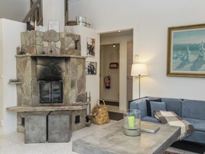 Uma sala de estar com lareira de pedra, um sofá azul, uma mesa de centro com uma vela e um quadro na parede.