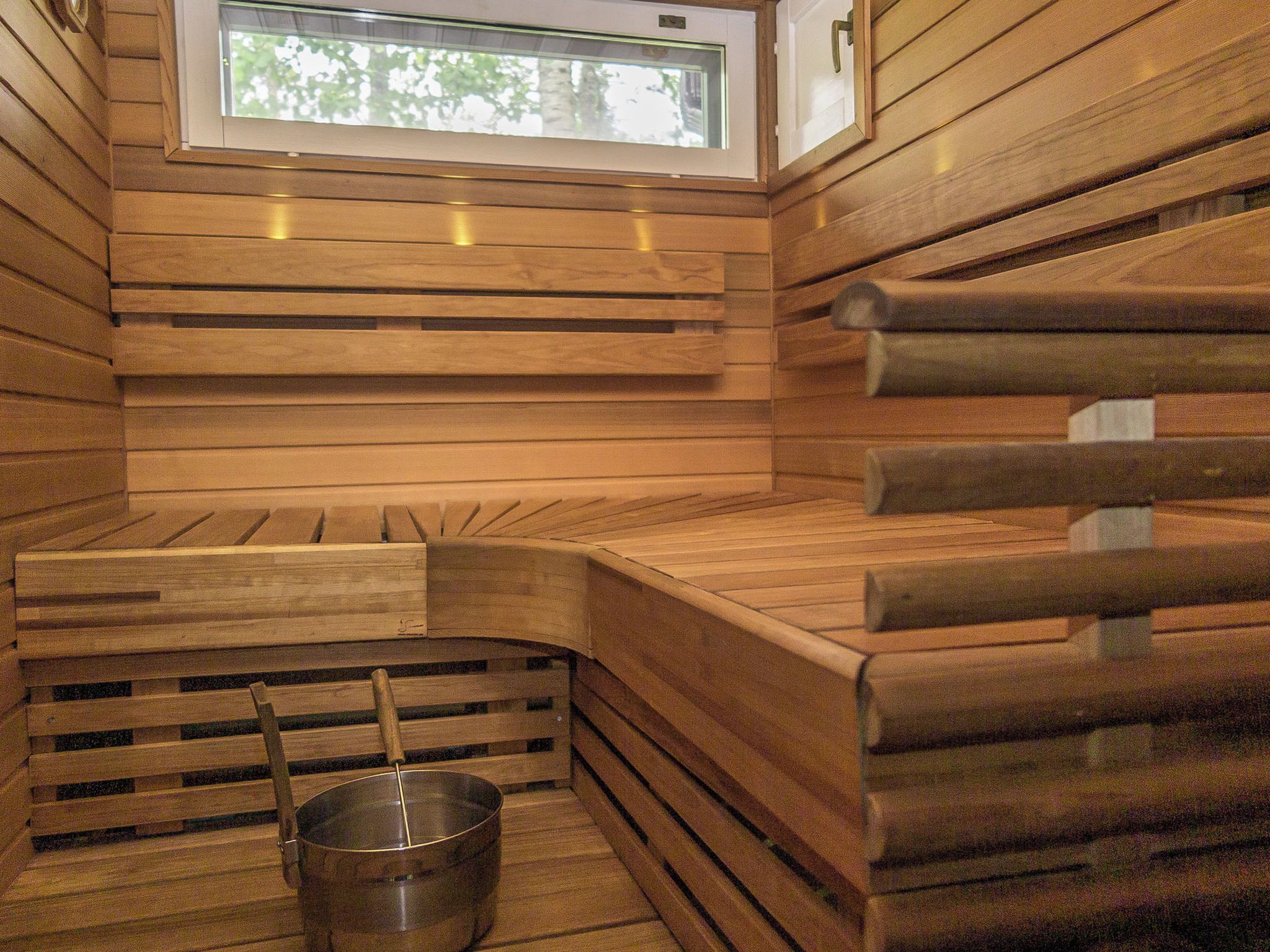 A sauna with wooden benches, a metal bucket, and a window.