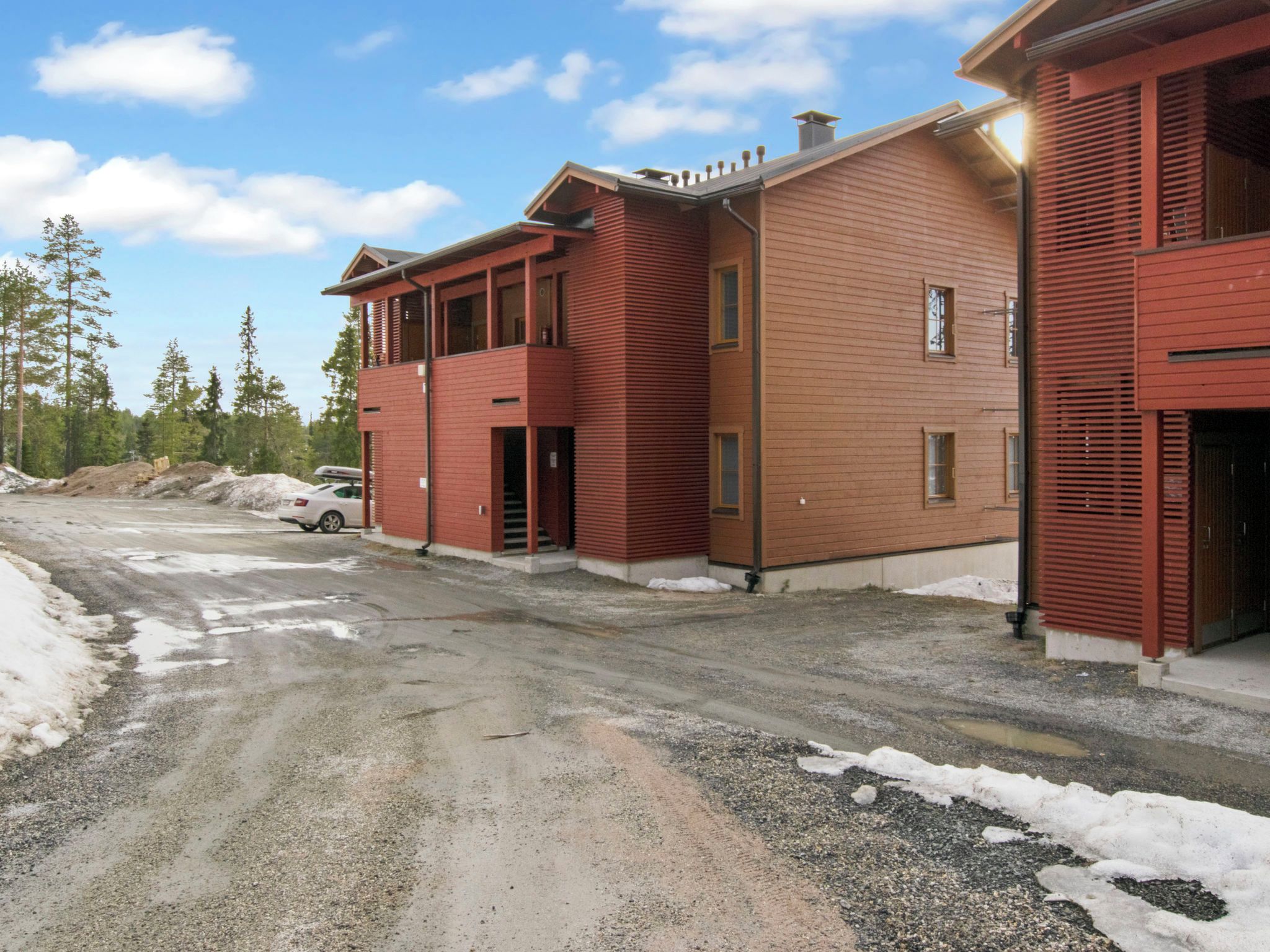 A multi-story building with a red exterior, a parking area with a car, and a snowy ground.