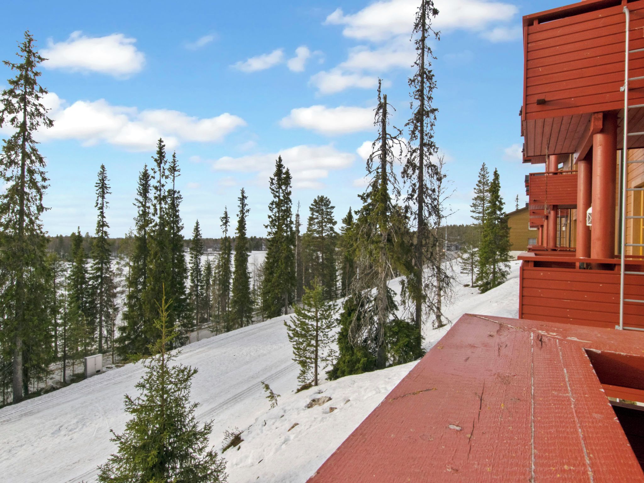 Punainen rakennus, jonka edessä on lumipeitteinen rinne ja taustalla metsä.