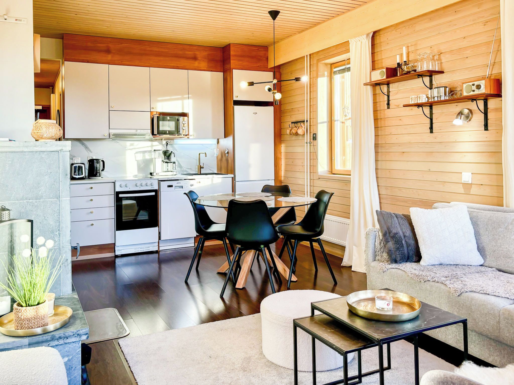 A modern kitchen with white cabinets, a microwave, and a refrigerator. There is a dining area with a table and chairs.