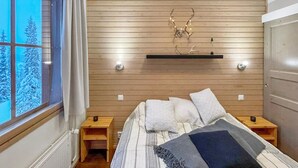 A bedroom with a wooden slat wall, a bed with multiple pillows, bedside tables, and a window with a view of snow-covered trees.