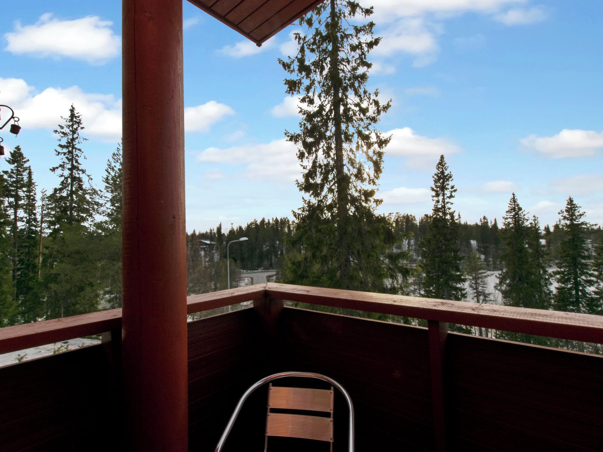 Une terrasse en bois avec une chaise en métal, donnant sur une zone boisée sous un ciel dégagé.