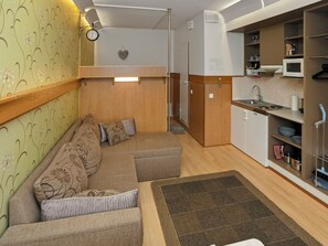 Un espacio habitable compacto con sofá, zona de cocina y una pequeña mesa de comedor.