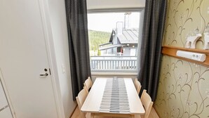 A room with a wooden table and chairs, a window with curtains, a door, and a wall with a floral pattern. - Snowflake b 24 by Interhome (Kuusamo)