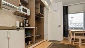 A compact kitchen with a refrigerator, microwave, and coffee maker. There is a dining area with a table and chairs, and a window with a view of the roof. - Snowflake b 24 by Interhome (Kuusamo)