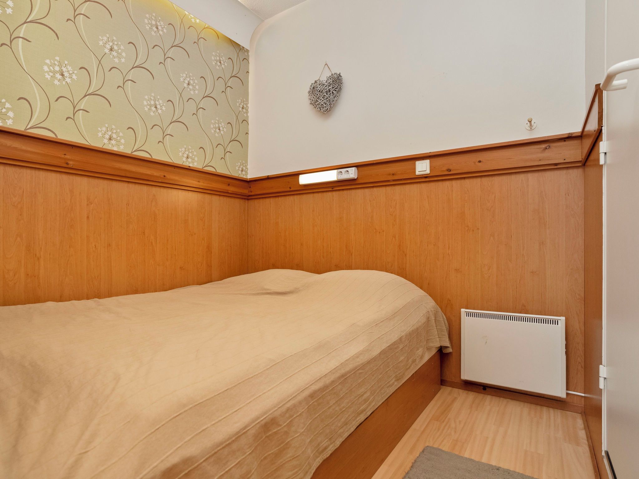 A small, single-bed room with wooden paneling, a radiator, and a wall-mounted light fixture.