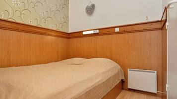 A small, single-bed room with wooden paneling, a radiator, and a wall-mounted light fixture.