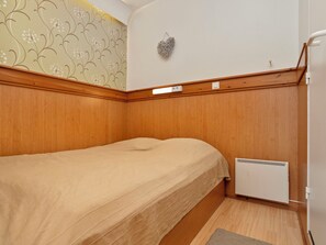 Una habitación pequeña con cama individual, paneles de madera, un radiador y una lámpara fijada a la pared.