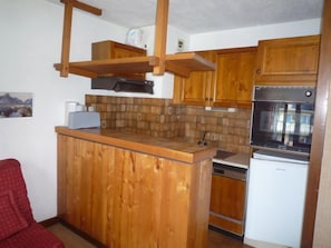 Eine kleine Küche mit Holzausstattung, einer eingebauten Mikrowelle und einem Edelstahlbackofen.