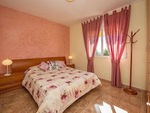 A bedroom with a bed, two bedside lamps, a window with curtains, and a coat rack.