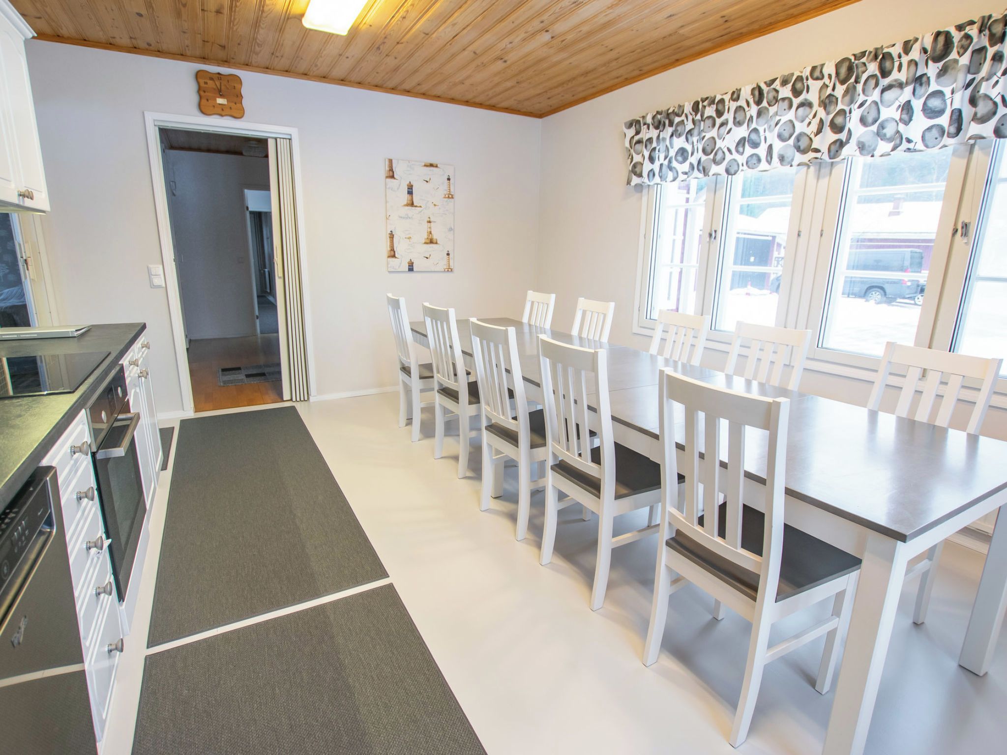 A dining area with a table and chairs, a kitchen with appliances, and a hallway leading to another room.
