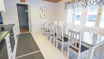 A dining area with a table and chairs, a kitchen with appliances, and a hallway leading to another room.