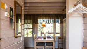 A wooden interior with a dining table, chairs, a radio, and a window with curtains.