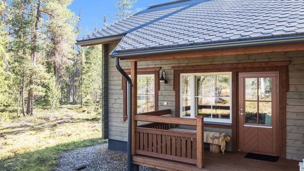 A cabin with a wooden deck, large windows, and a metal roof.