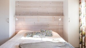A bedroom with a bed, two bedside lamps, and a wooden ceiling.