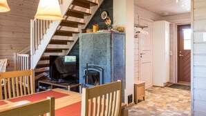 A cozy living room with a fireplace, wooden staircase, and a dining area with red mats.
