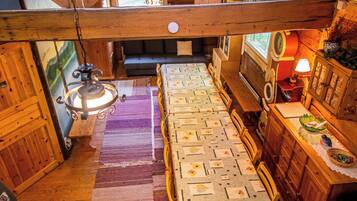 A cozy cabin interior with a wooden ceiling, a bed with floral bedding, a dining table, and a window with curtains.