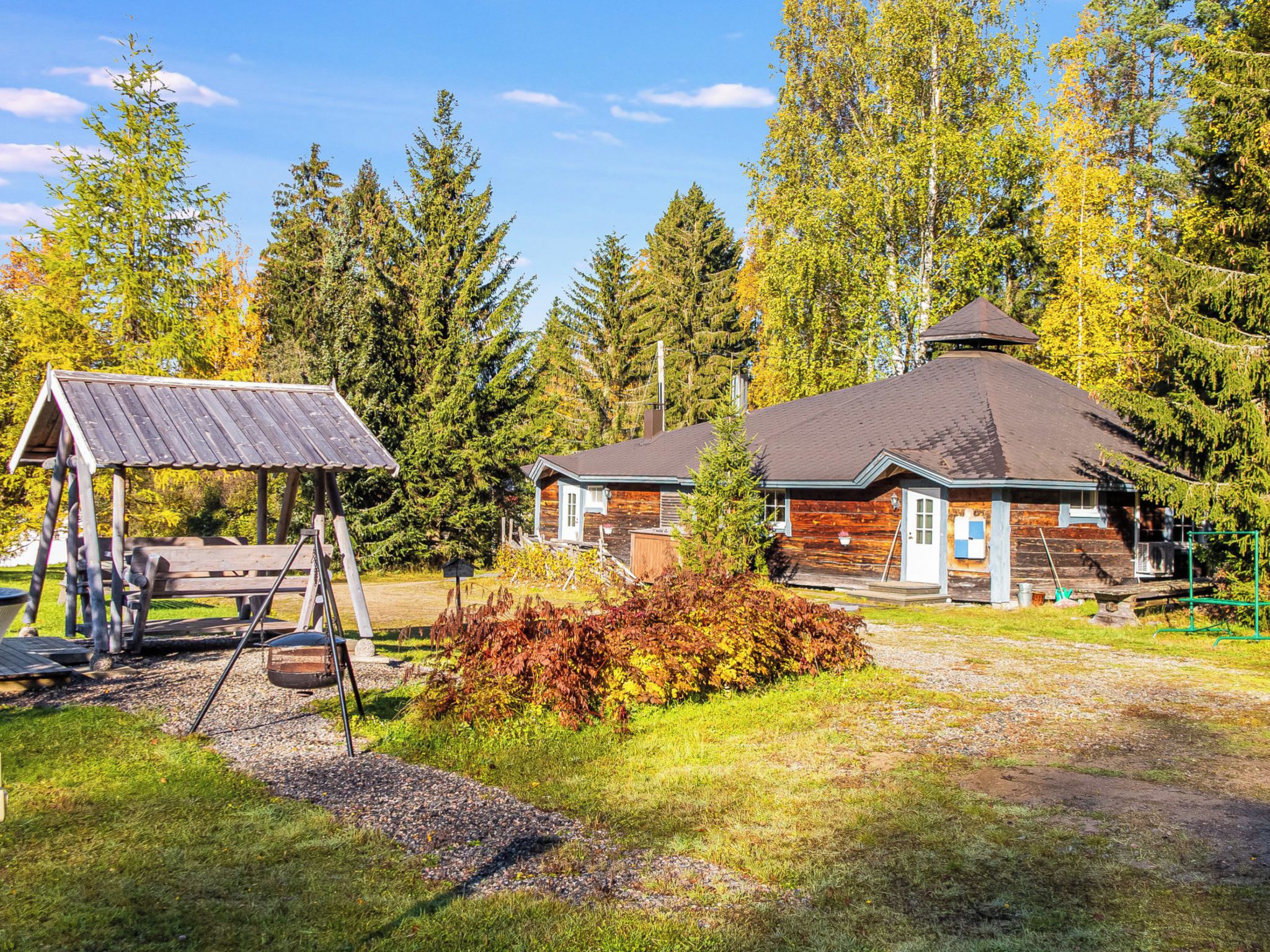 En stuga med träfasad, en lekplats under tak och en välskött trädgård.