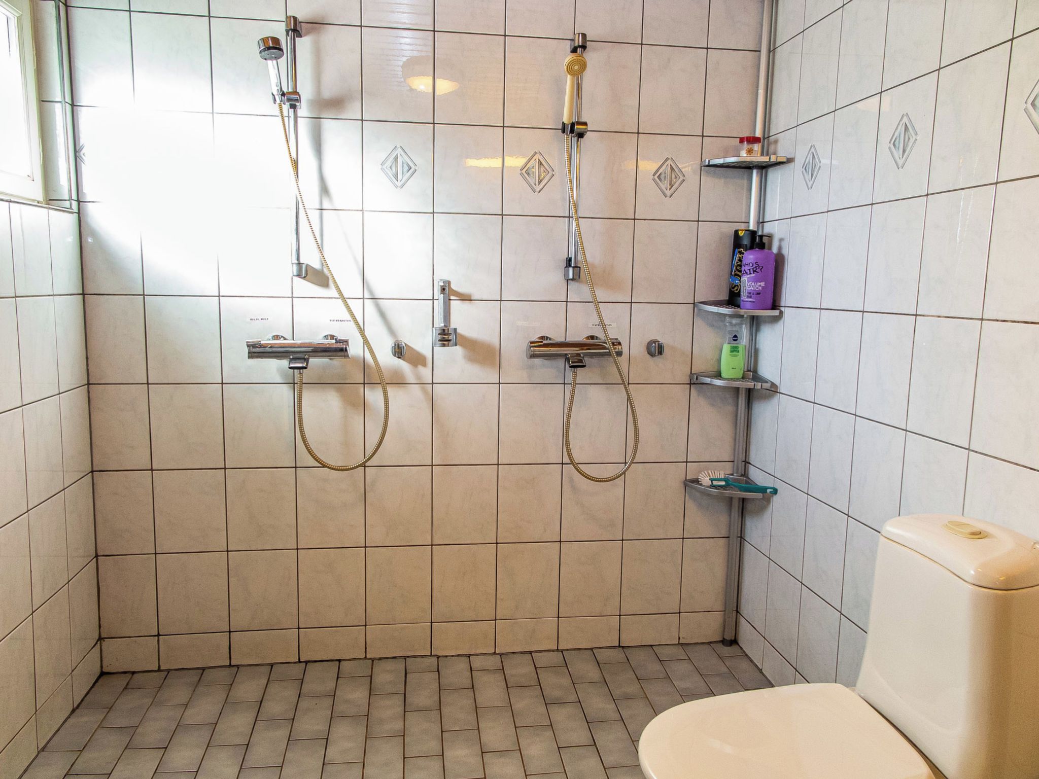 Un baño con ducha, inodoro y estantes con art ículos de aseo.
