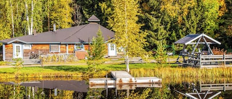 A cabin with a dock extending into a calm lake, surrounded by dense forest.