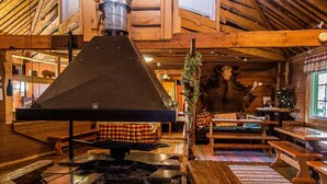A rustic lodge interior with a stone fireplace, wooden furniture, and a high ceiling with exposed beams. - Kuusenkatve by Interhome (Nilsiä)