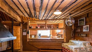 A rustic wooden interior with a wooden ceiling, a kitchen area with a window, a disco ball, and a table with a checkered tablecloth. - Kuusenkatve by Interhome (Nilsiä)