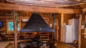 A rustic wooden interior with a large black stove, wooden benches, a small table, and a refrigerator. - Kuusenkatve by Interhome (Nilsiä)