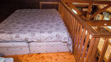 A small, cozy room with a wooden floor, a single bed with a patterned mattress, and a wooden railing.