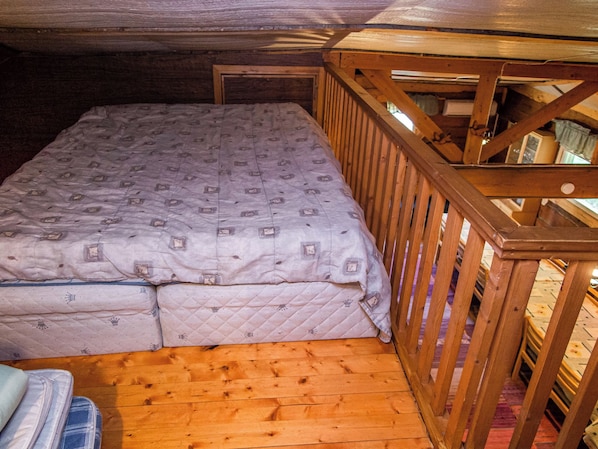A small, cozy room with a wooden floor, a single bed with a patterned mattress, and a wooden railing.