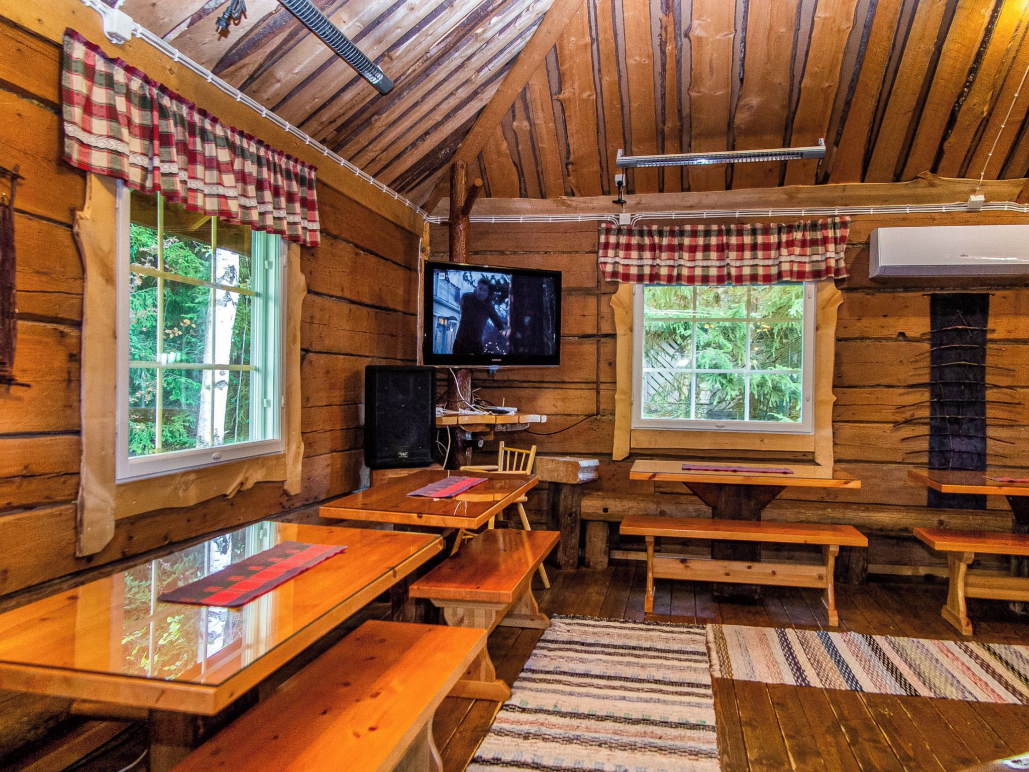 Ein rustikales Blockhaus-Interieur mit Holzwänden, einem Fernseher und mehreren Holzbänken.