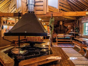A rustic interior with a wood-burning stove, wooden furniture, and a stone fireplace.