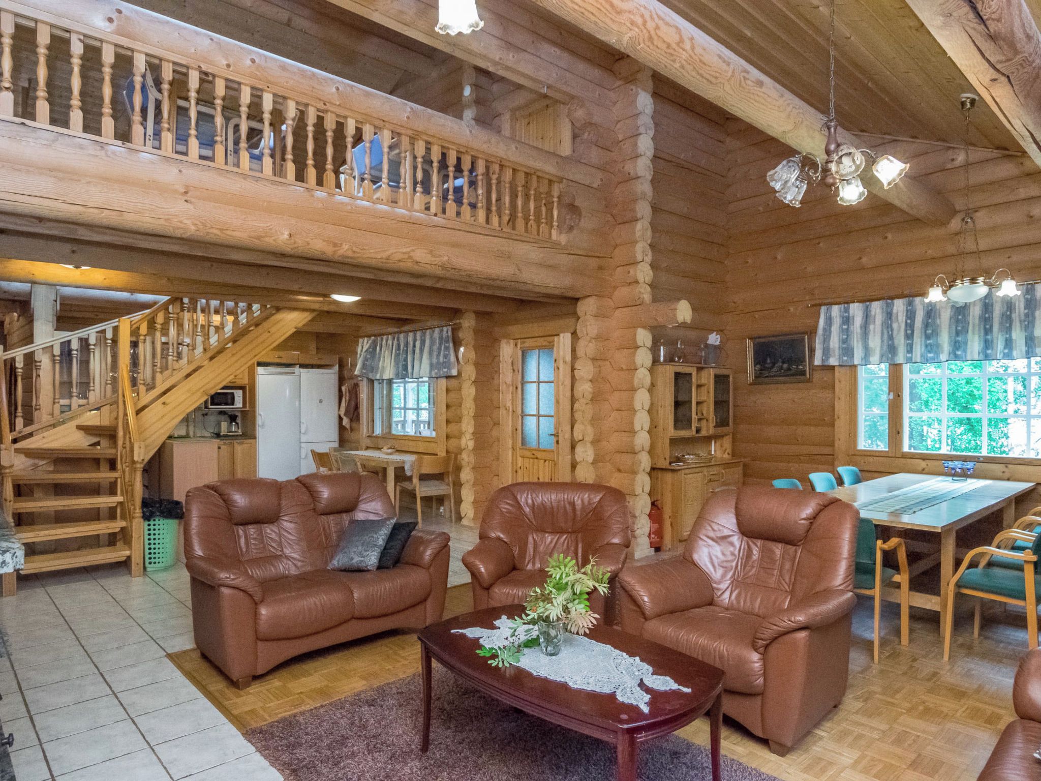 A log cabin interior with a staircase, leather sofas, a dining table, and a kitchen area.