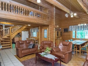 A log cabin interior with a staircase, leather sofas, a dining table, and a kitchen area.