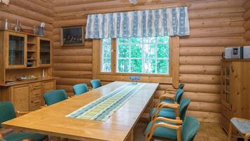 L’intérieur d’un chalet en bois comprend une table à manger, des chaises, un coin cuisine et une fenêtre donnant sur un paysage verdoyant.