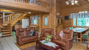 A log cabin interior with a dining area, two leather sofas, a staircase, and a kitchen.