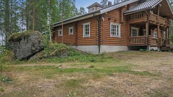 Une cabane en rondins dotée d’une véranda, entourée d’un paysage naturel.
