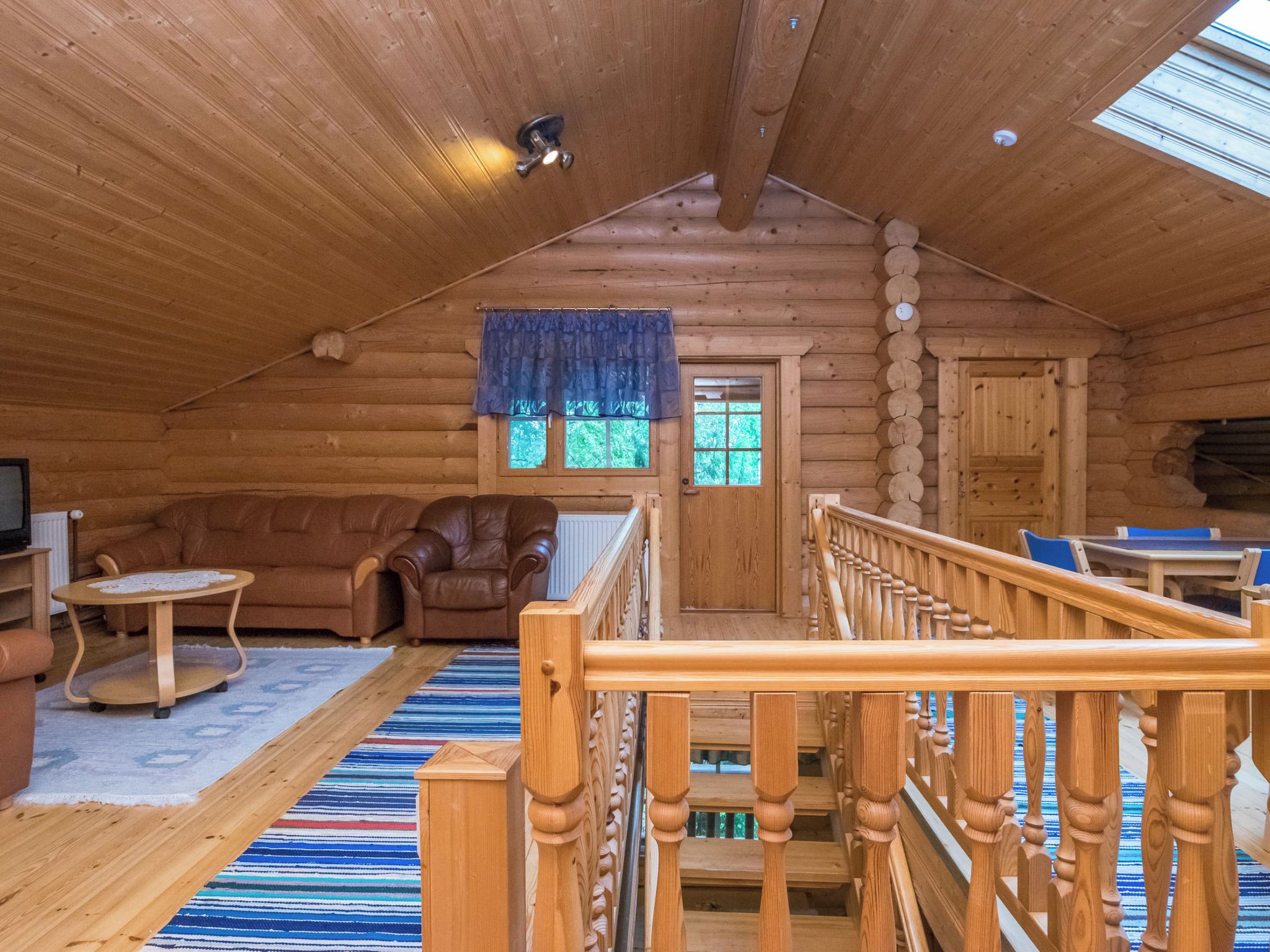 Interior de uma cabana de tronco com escada de madeira, sofá de couro e uma pequena mesa.