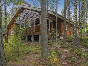A log cabin with a glass extension, surrounded by trees and a forest floor.