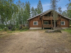 Une cabane en rondins avec un porche, entourée d’arbres.
