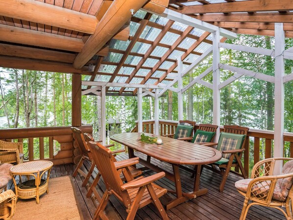 A wooden deck with a covered patio area, furnished with wooden chairs and a table.
